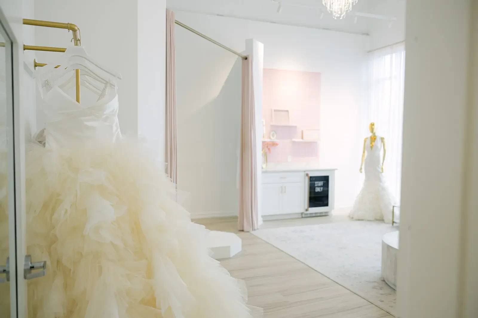 Elegant bridal shop interior with a flowing, ruffled wedding dress on a rack. Soft pink curtains and a mannequin create a serene, romantic ambiance.