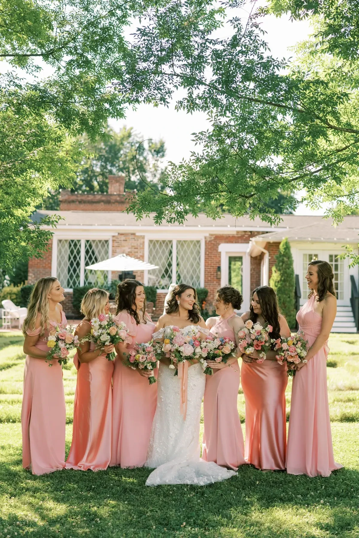 A bride smiles at her bridesmaids wearing beautiful light pink bridesmaid dresses and colorful floral bouquets in hand