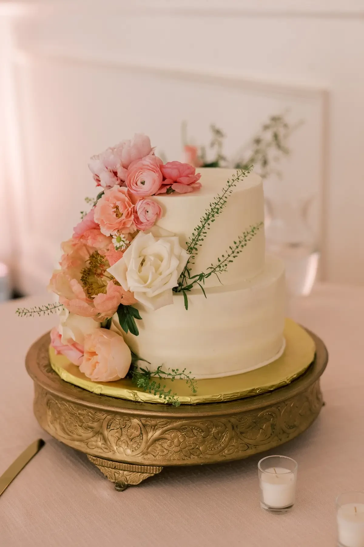 Image shows a white wedding cake with blush pink roses and greenery