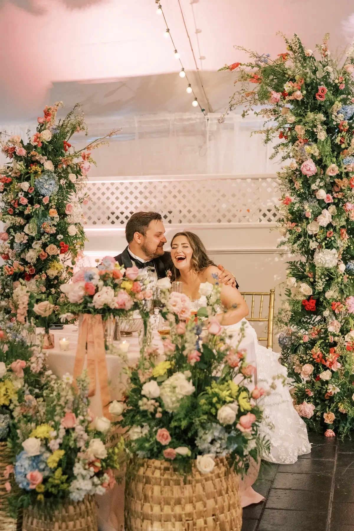 A groom looks lovingly at his wife as she laughs on their wedding day in an array of blooming flowers around them