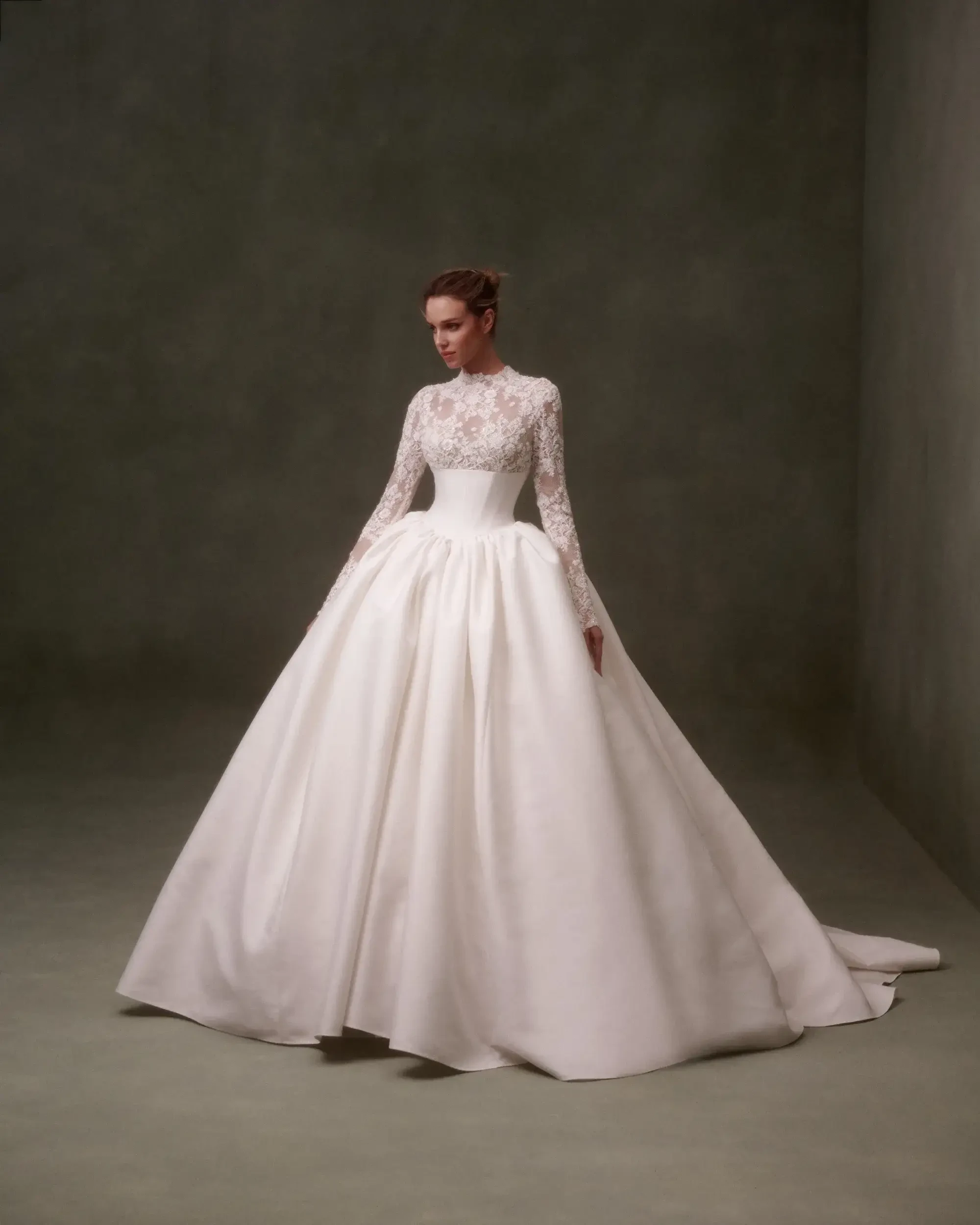 A model wearing an elegant white ball gown with long sleeves and intricate lace detailing, posed against a muted background.