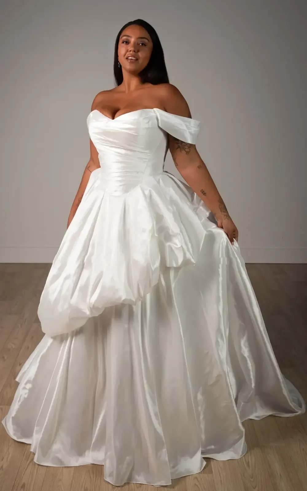 A person wearing a strapless, off-the-shoulder white dress, standing and smiling.