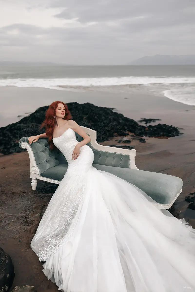 Model wearing a white gown laying on a chair on the beach